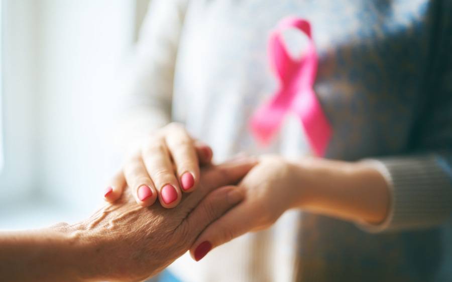 Inflammatory breast cancer patient holds hand of supporter who is wearing a cancer ribbon.
