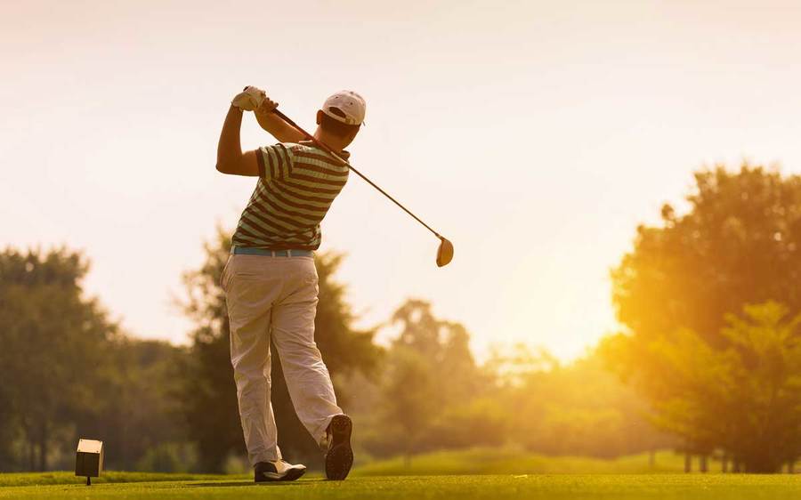 A golfer in silhouette takes a swing on a well-maintained golf course in late afternoon