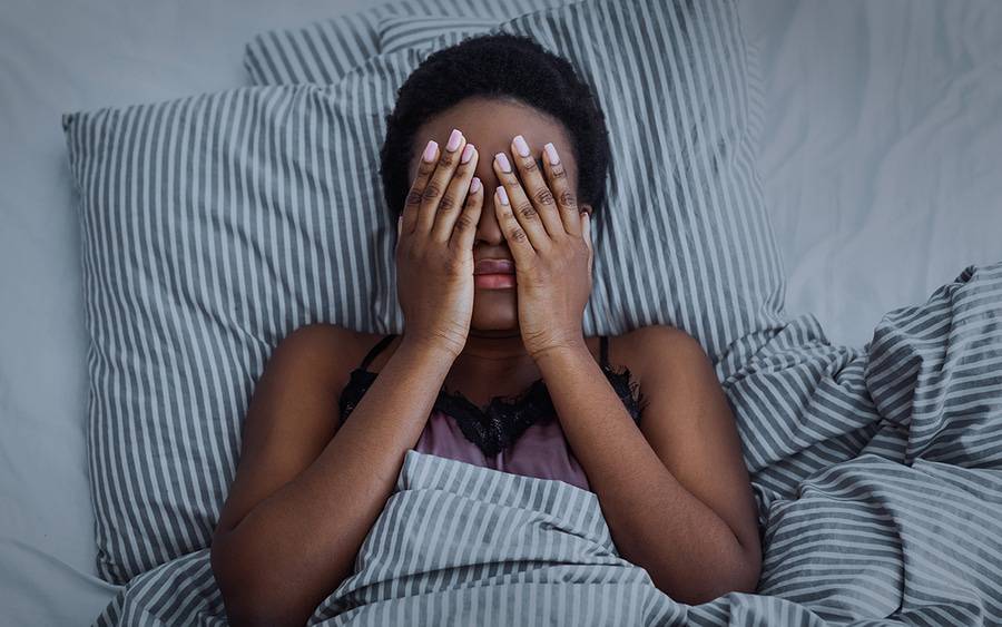 An African-American woman rubs her eyes while struggling to fall asleep because of her insomnia.