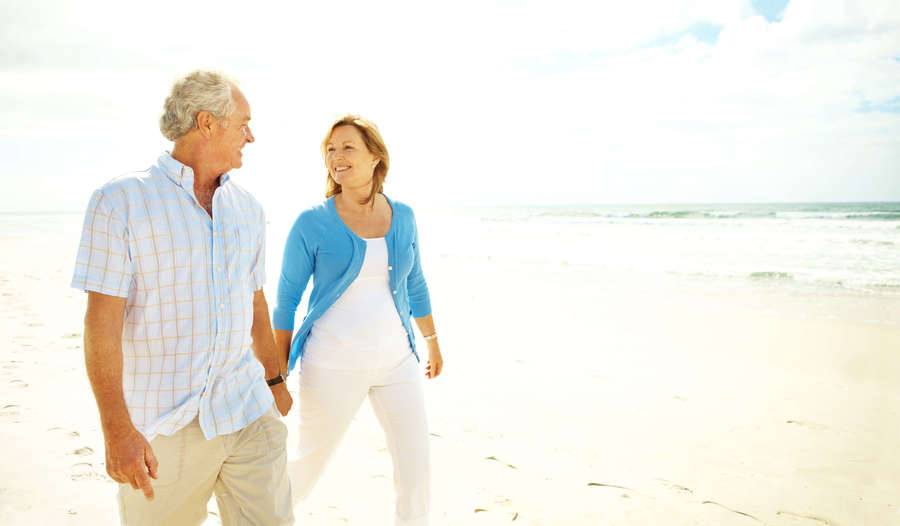 A mature couple holds hands as they walk down the beach.
