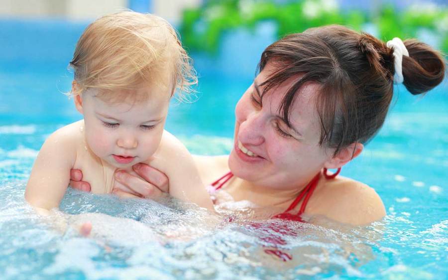 A happy mother splashes in the pool with her infant during a swim lesson.