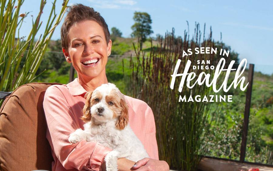 Kelly O'Connor smiles at home outdoors holding her small dog after breast cancer treatment. SD Health Magazine