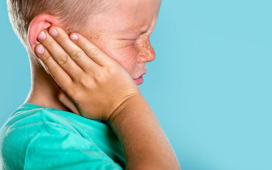 A young child winces in pain from an ear infection.