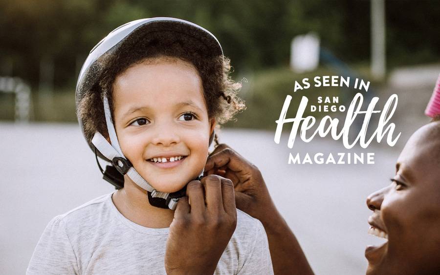 A parent straps a helmet on our smiling boy. San Diego Health Magazine