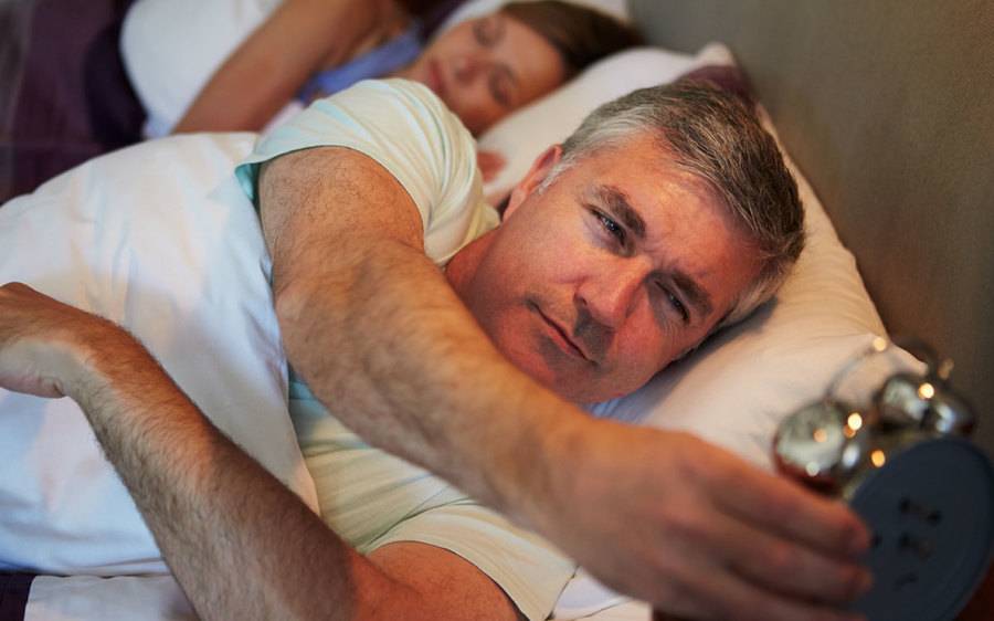 A mature man sets his alarm clock as one way to get a better night's sleep.