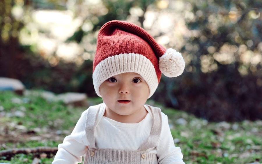 Baby Leo Dakin celebrates his first Christmas at home. He wears a Santa hat while sitting outdoors on the grass in his family's backyard.