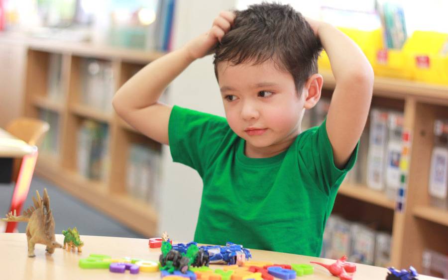 A child with head lice scratches his head at a play table.