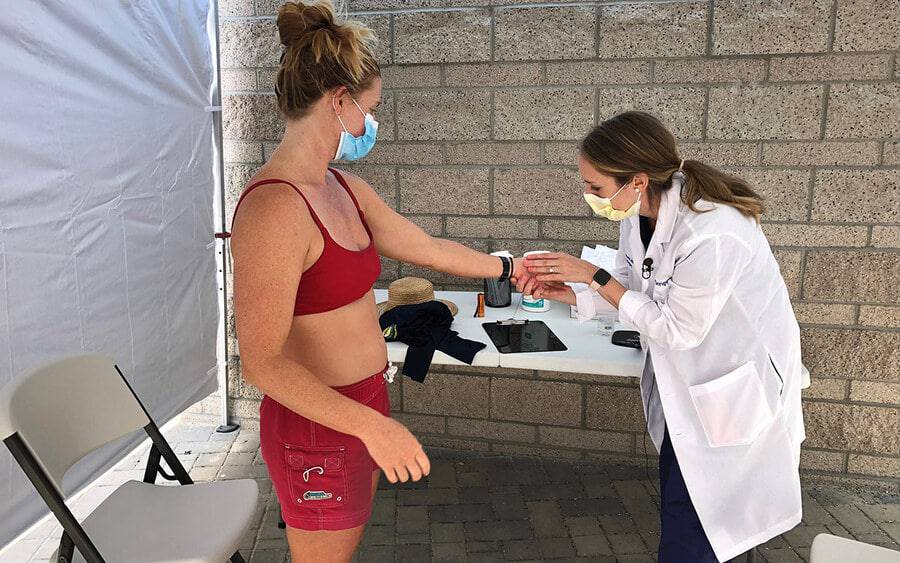A lifeguard receives skin cancer screening outdoors by a medical professional.
