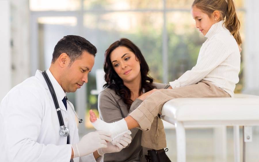 A family medicine physician checks a girl's injured foot.
