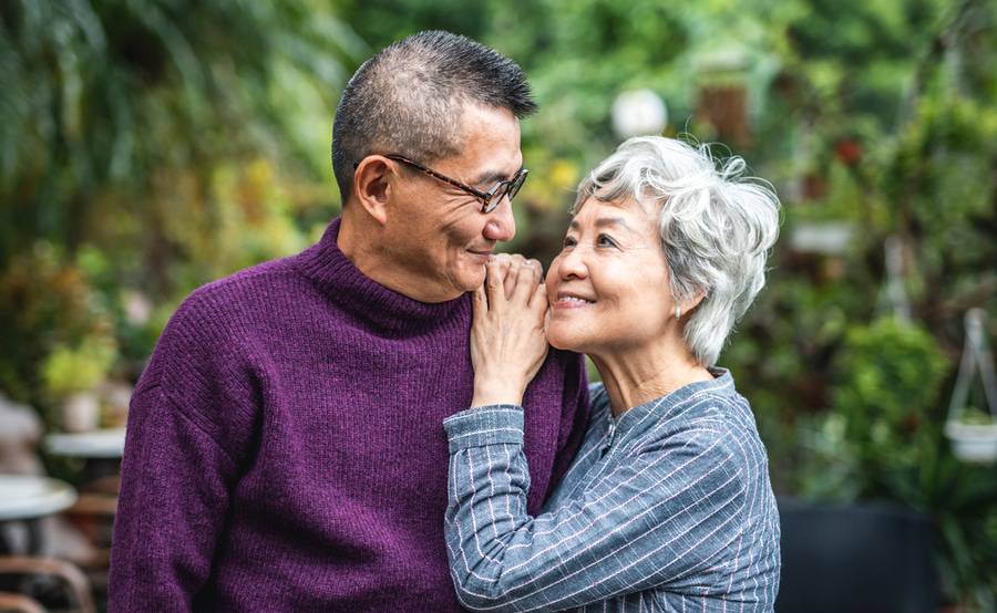 An older couple looking at each other and smiling in an outdoor garden.