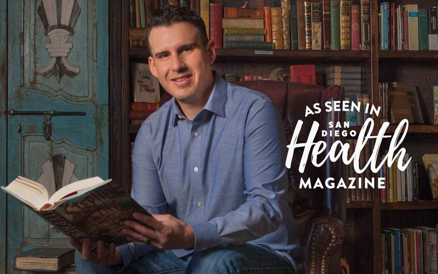 A man reads a Stephen Kind hardback book in a library filled with classics.