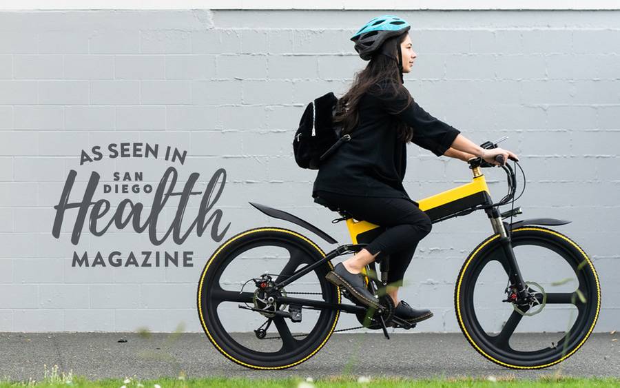 A young woman riding a yellow and black electric bike, wearing a protective helmet and small backpack.