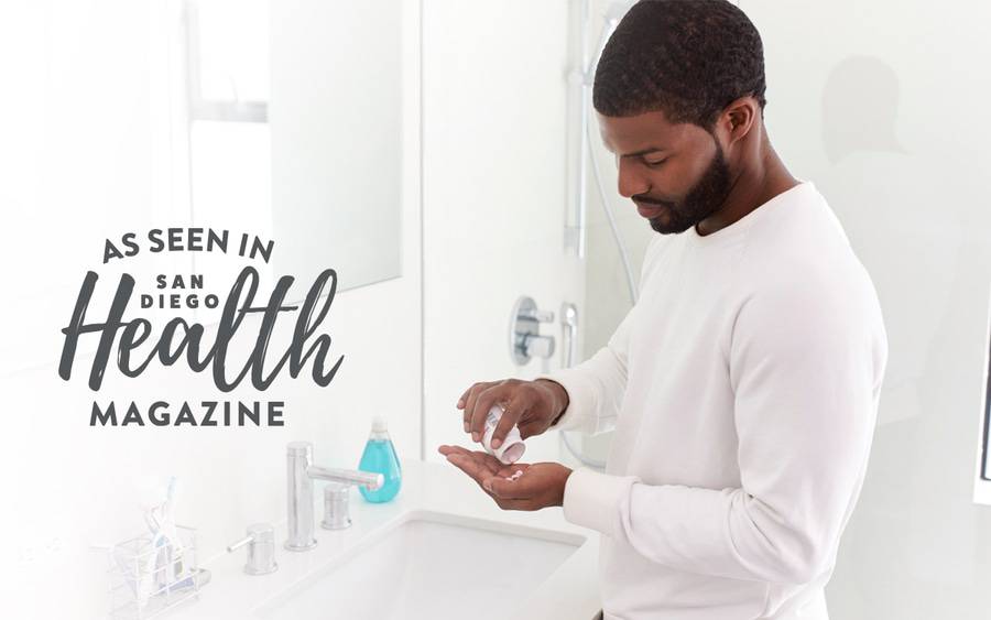 A man stands by a bathroom sink, tipping a dietary supplements from a bottle into his palm.