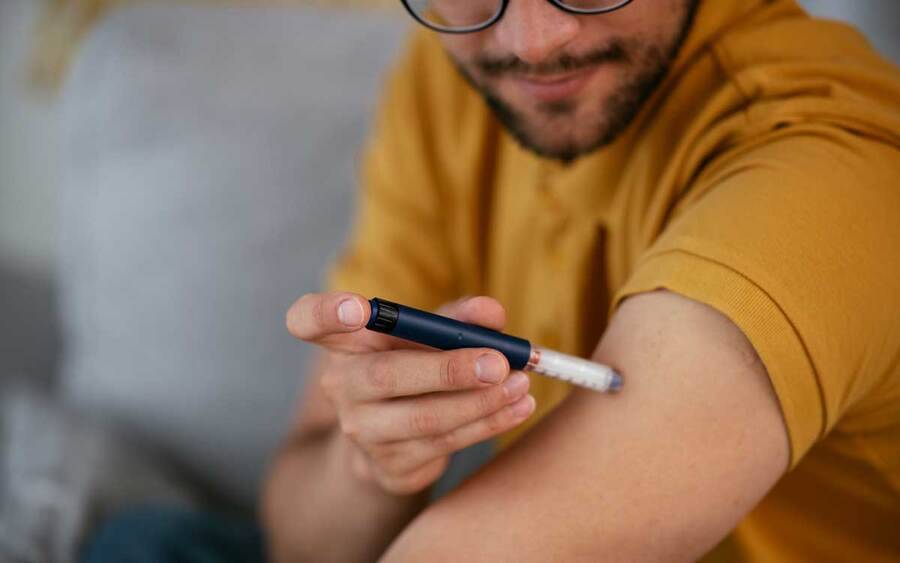 A man with glasses and a yellow shirt is injecting insulin into his arm.