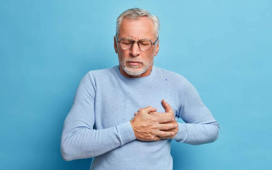 A man clutches his chest in pain, experiencing a heart attack that needs immediate medical attention.
