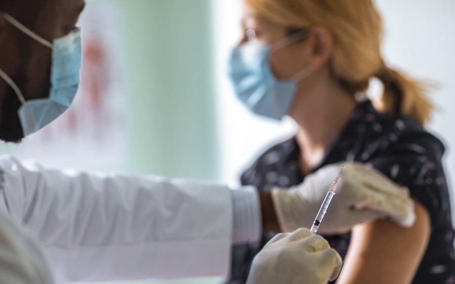 A provider wearing a mask and holding a flu shot while administering it to a patient also wear a mask.