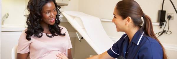 A pregnant woman and a health care provider smiling and sitting together in an examination room, representing warm and compassionate maternity care at Scripps.