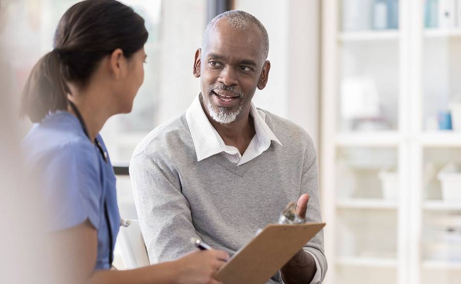 A mature male patient is discussing his health with a provider documenting the visit, illustrating the care provided by XiMED Medical Group providers.