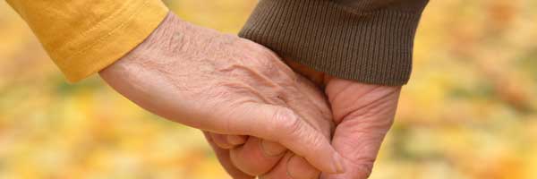 Close up shot of an elderly man and woman holding hands in an outdoor autumn setting