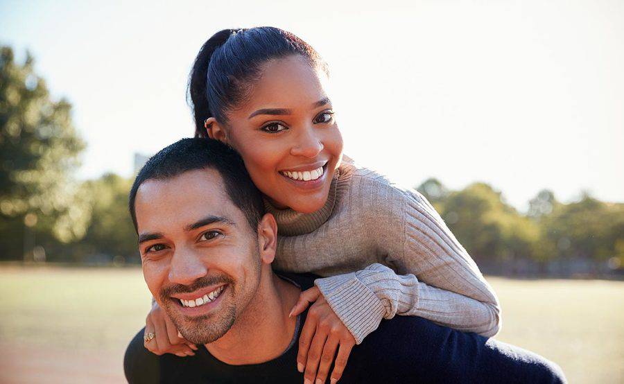 A smiling young woman gets a piggyback from a young man, representing the full life that can be led with skin disease treatment.