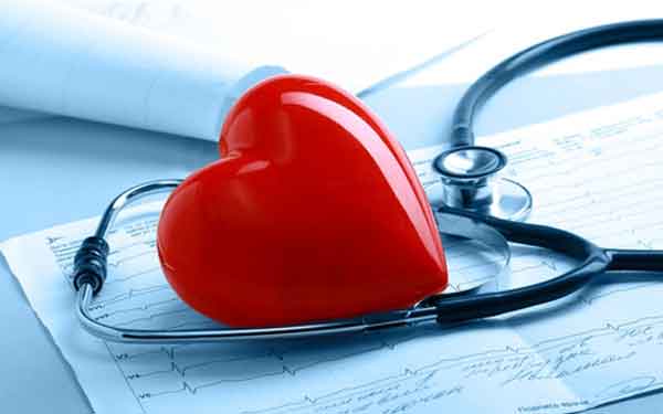A red heart is in the center of a stethoscope on top of an electrocardiogram on a desk.