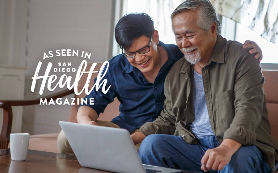 A young Asian man helps his senior aged father compare Medicare plans on a laptop computer.
