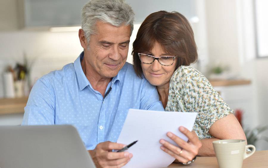 Older couple in their home near a computer over looking some paperwork.
