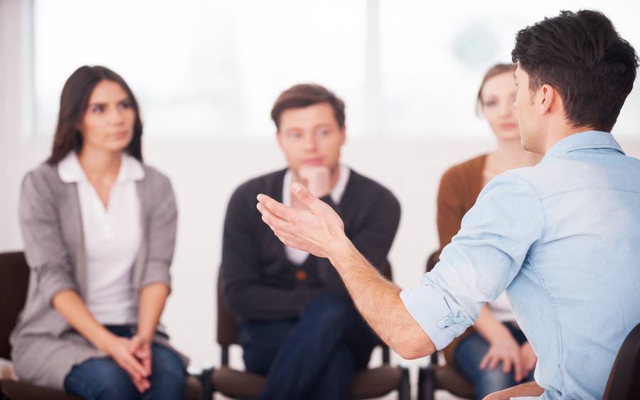 A young man talks to a group of adults, representing a support group for friends and family of people with mental health conditions. 