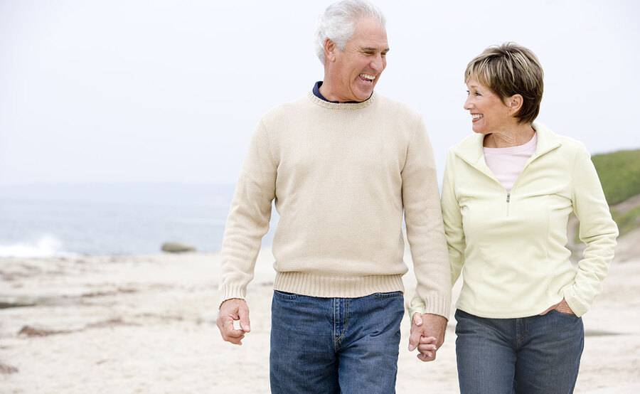 A middle-aged couple walks along the beach, holding hands.