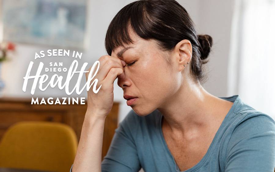 A middle aged Asian woman touches her sinuses with her eyes closed. San Diego Health Magazine