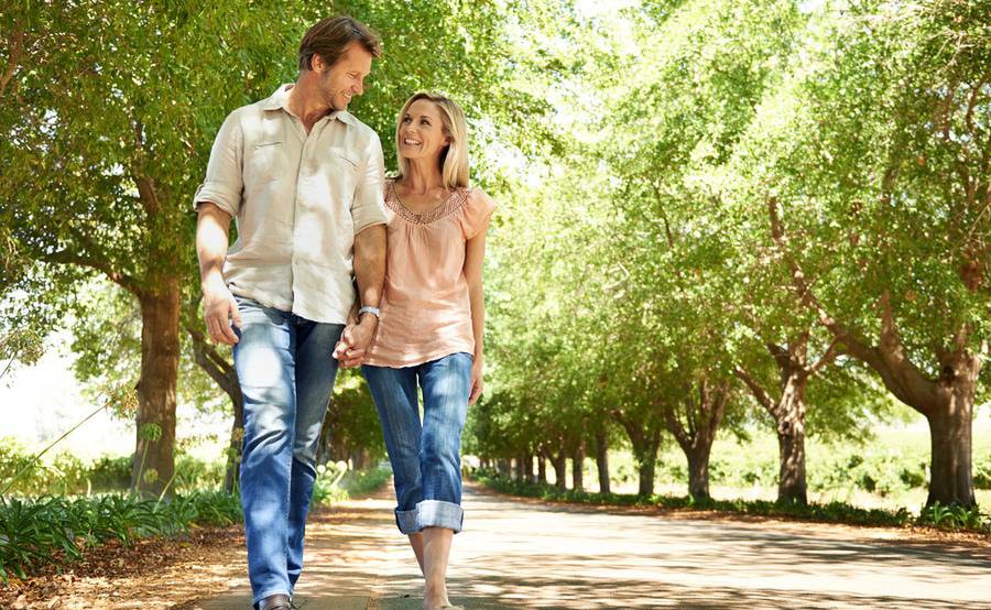 A couple holding hands while walking under sunlit trees beside a country road, representing the quality of life that robotic surgery can help people enjoy.