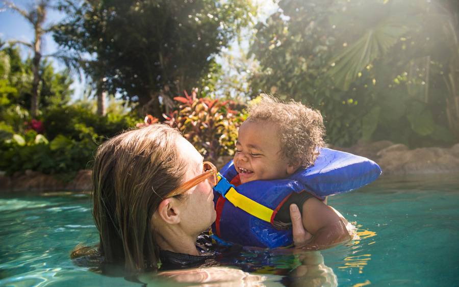 A mom and her baby who is wearing a life vest play in the pool.