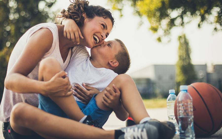 A mother smiles and her son kisses on the cheek, A basketball by their side suggests he's been active during spring break from school.