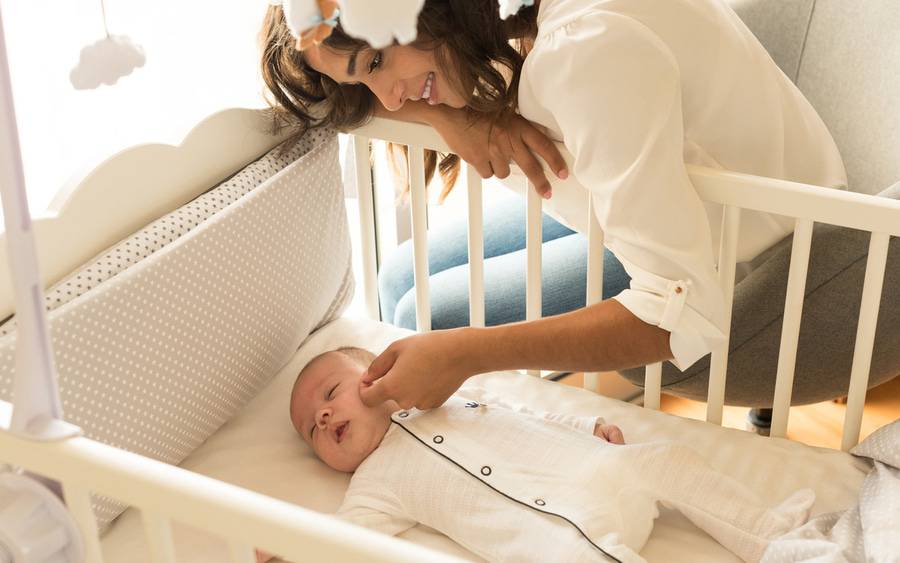 A mom caresses baby who has just fallen asleep in his crib.