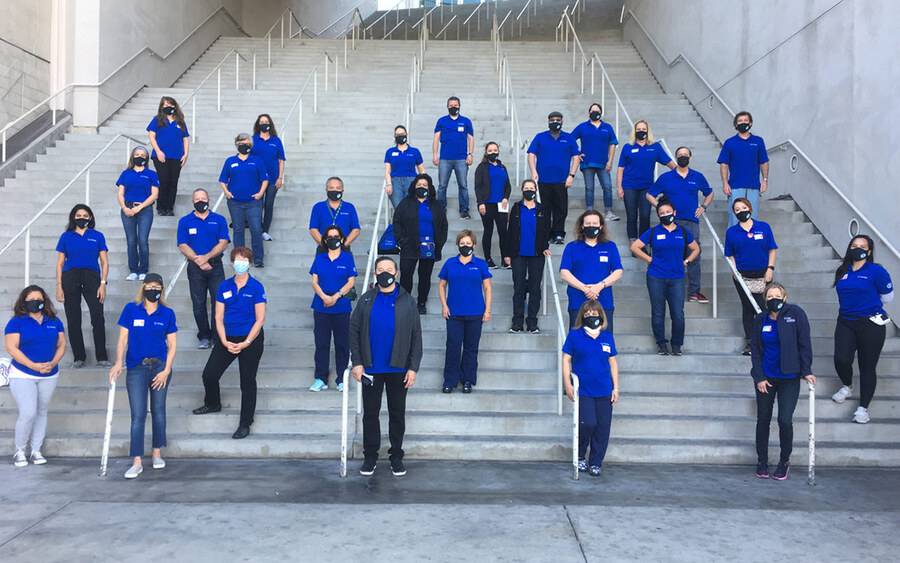 Volunteers from M.O.S.T pose on a large outdoor stairway wearing medical masks during the COVID pandemic.