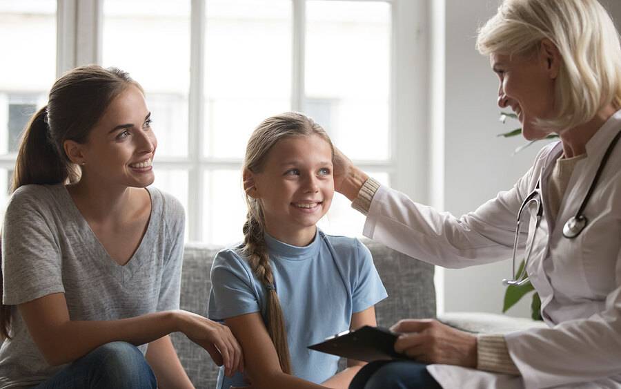 A mom and her daughter smiling as her daughter's Pediatrician is consulting with them.