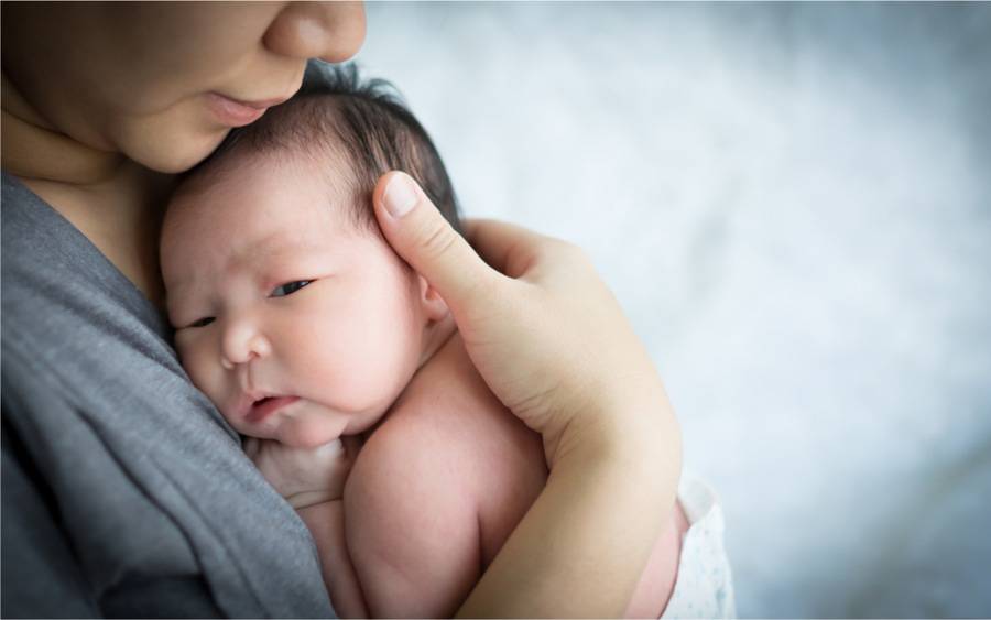 A mother holds her newborn baby daughter close to her chest.