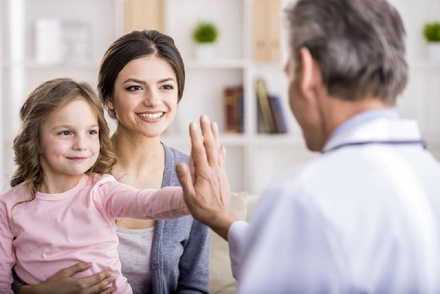 Doctor touches little girl's hand while mom watches.
