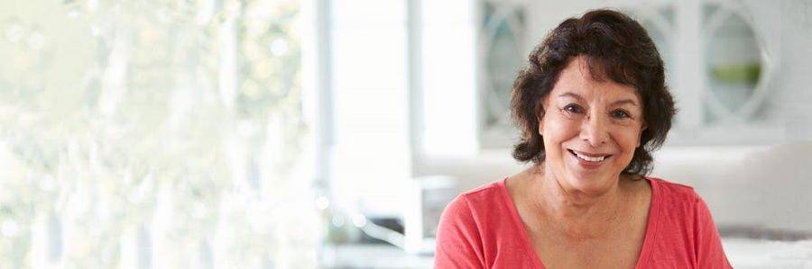 A happy middle-aged woman relaxes in a brightly lit kitchen setting.