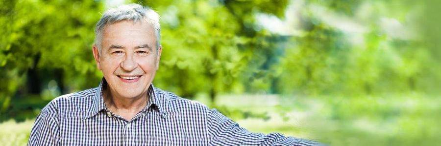 A happy elderly gentleman rests on a bench in a pleasant garden setting.