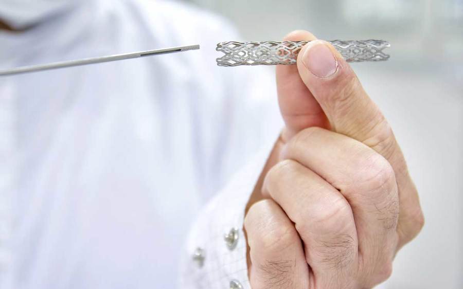 A doctor wearing a lab coat holds a heart stent