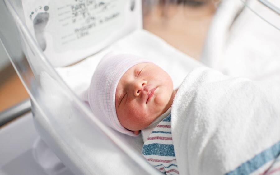 A  newborn baby, wrapped and sleeping  in hospital bed.