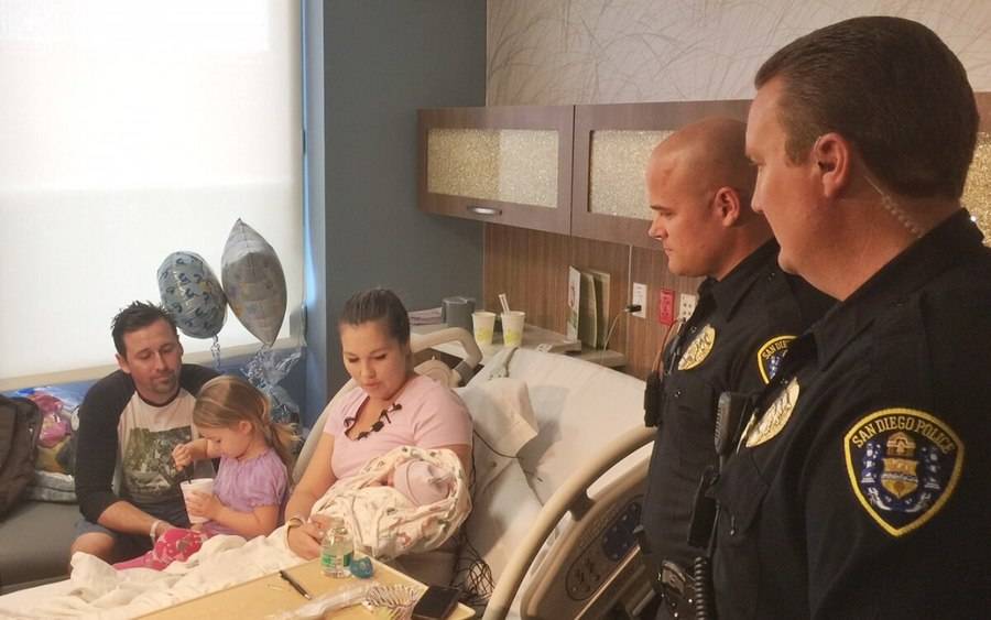 A new mother sits with her young family in the hospital room with the male police officers who helped deliver her baby.