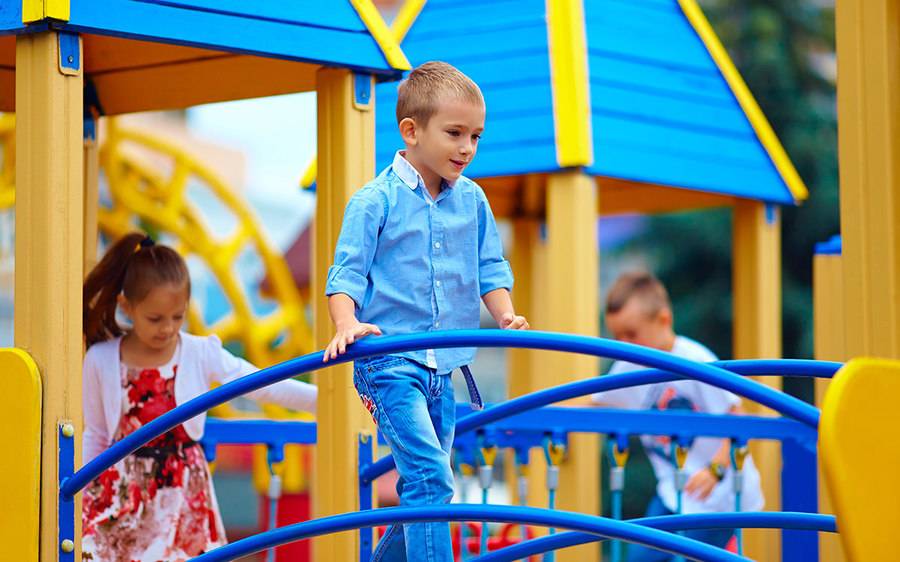 A young boy in a blue shirt and jeans plays nicely with other kids at a playground, showing how not to be a bully.