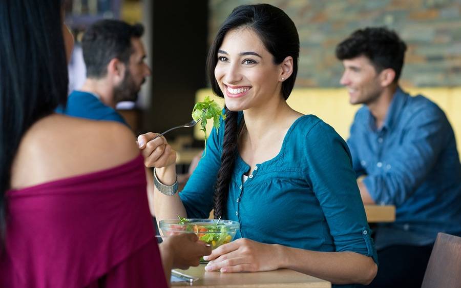 A healthy and attractive woman eats salad while enjoying the company of her girlfriend in a busy restaurant.