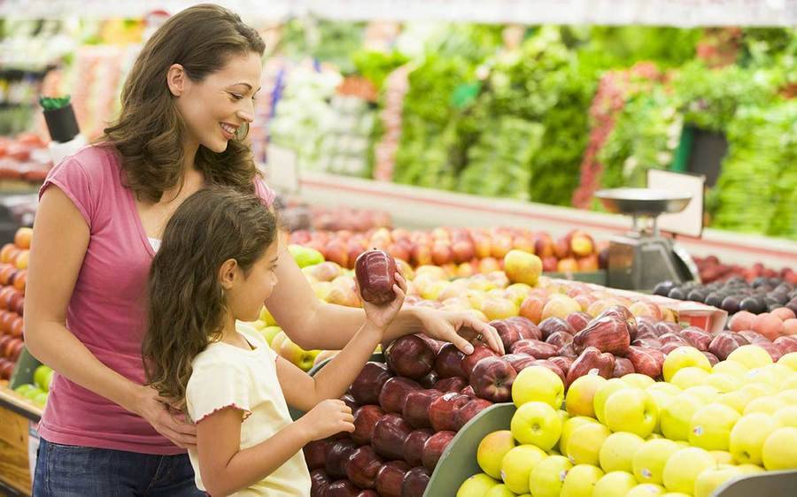 A mother and her daughter pick an apple together to help the girl pack a healthier school lunch.