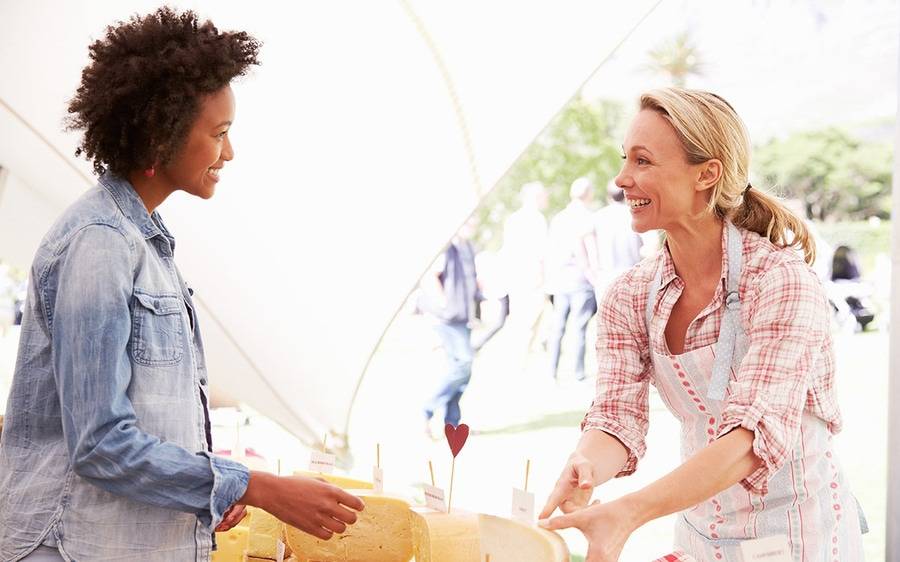 Two women discuss the savory aspects of organic cheese at a farmers market shopping event.