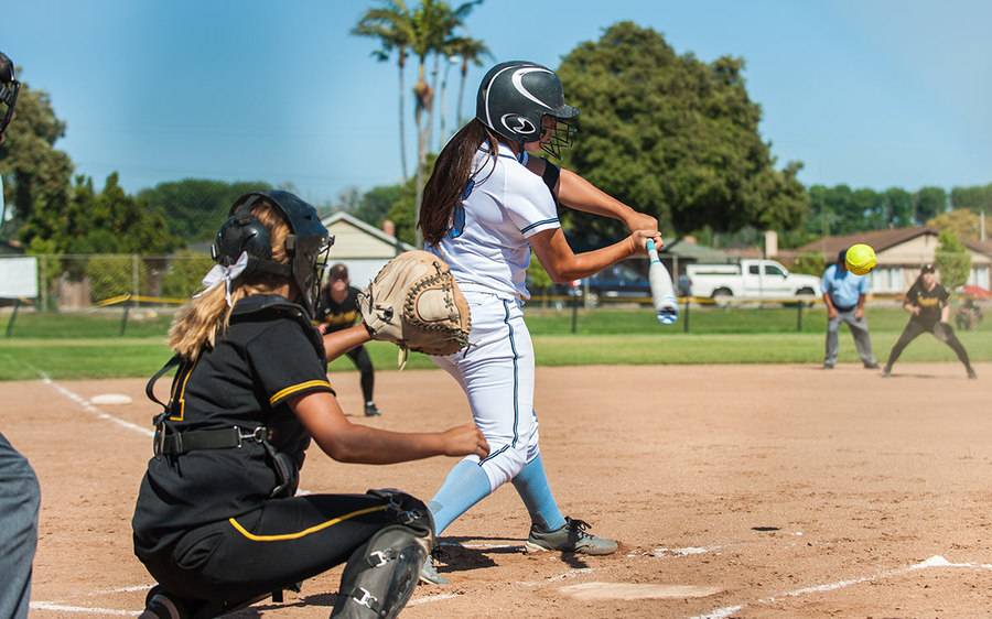 A young softball player prepares to hit a yellow softball during a game.