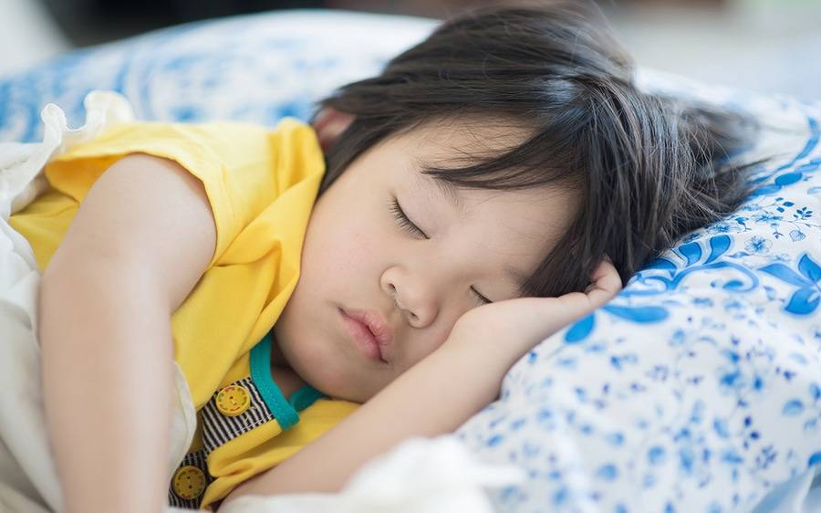 A toddler sleeps on a cozy blue and white pillow, getting much-needed rest,