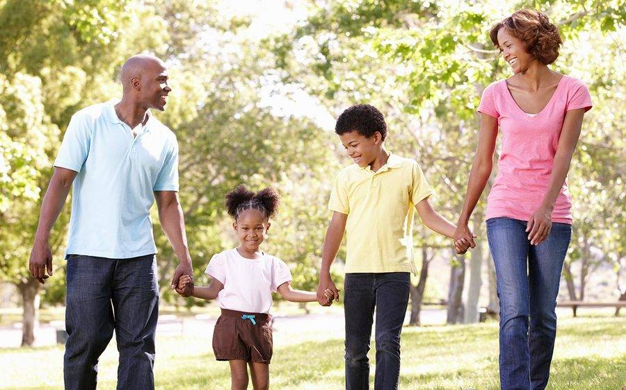 A young family of four enjoy a walk together during a sunny day at the park.